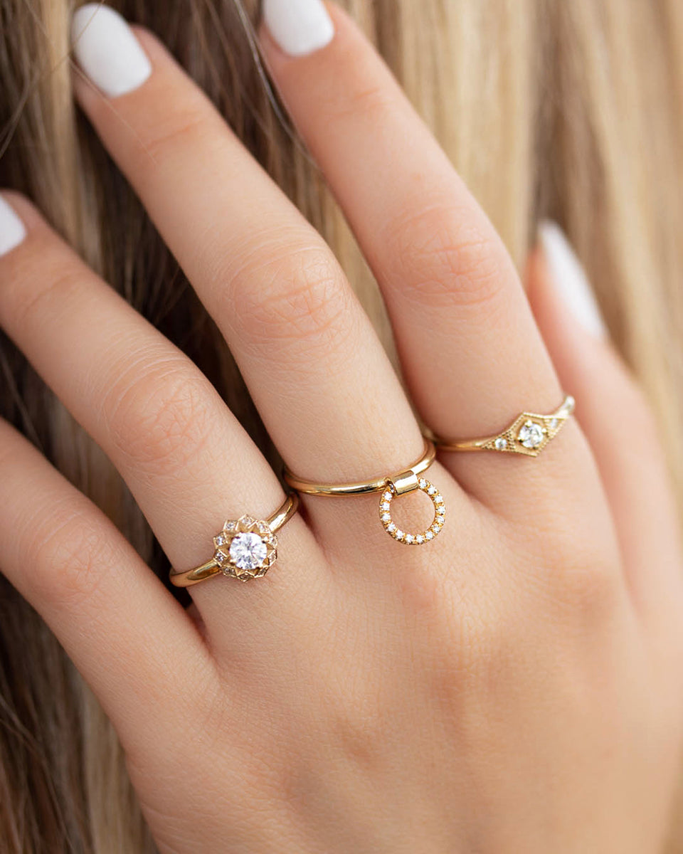 A delicate 14k yellow gold engagement ring, set with a center brilliant cut white diamond and smaller diamonds around it, in the shape of a geometric flower.