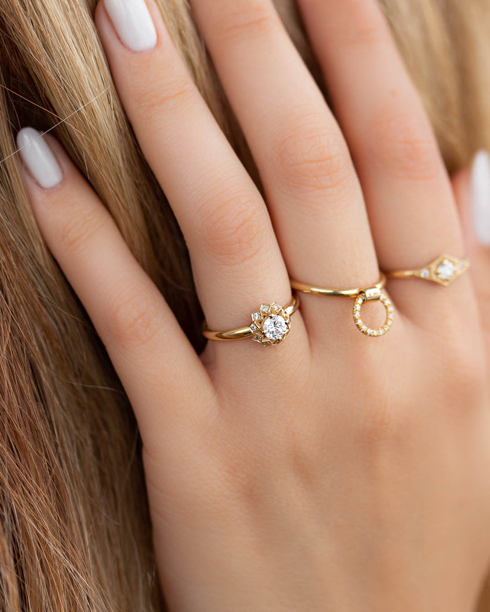 A delicate 14k yellow gold engagement ring, set with a center brilliant cut white diamond and smaller diamonds around it, in the shape of a geometric flower. 