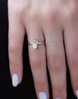 A 14k yellow gold engagement ring, set with a center pear cut white diamond and and halo of three small white diamonds.