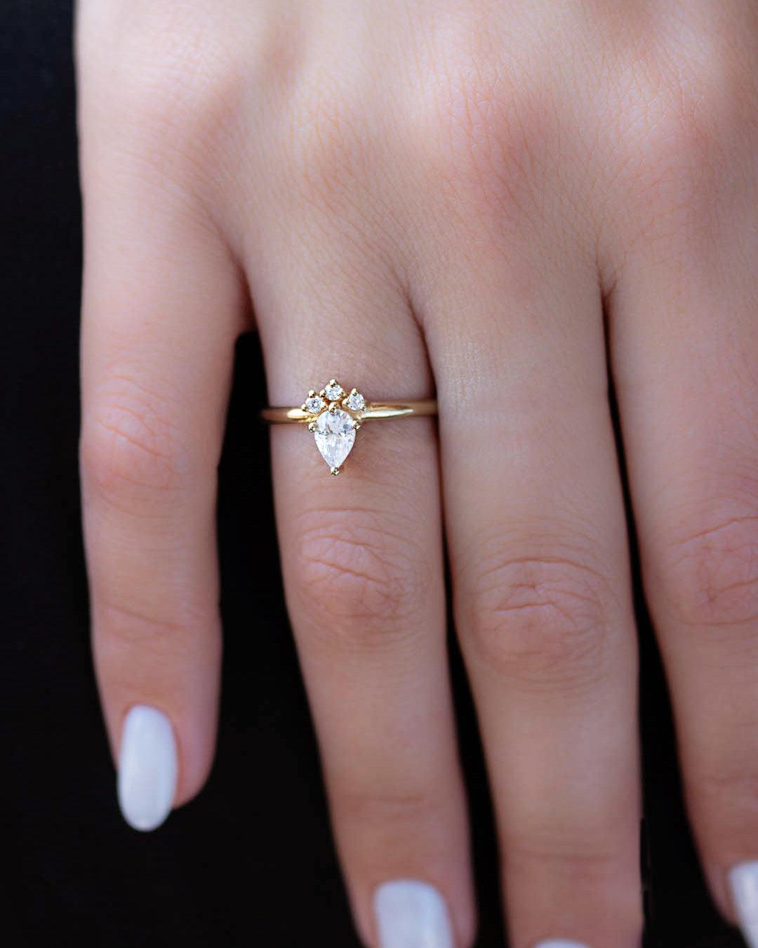 A 14k yellow gold engagement ring, set with a center pear cut white diamond and and halo of three small white diamonds.