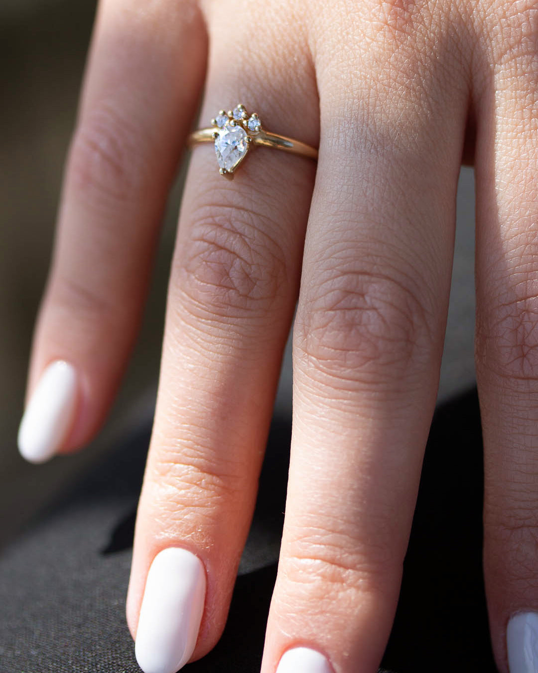 A 14k yellow gold engagement ring, set with a center pear cut white diamond and and halo of three small white diamonds.