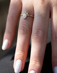 A 14k yellow gold engagement ring, set with a center pear cut white diamond and and halo of three small white diamonds.