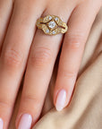 A close-up of a hand wearing an Art Deco style diamond ring. The ring features a central round diamond surrounded by geometric, beaded diamond bands in 14k yellow gold. 