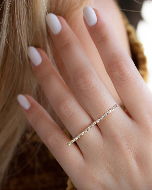 A dainty 14k yellow gold two finger ring, with a long bar set with white diamonds, that covers both fingers.