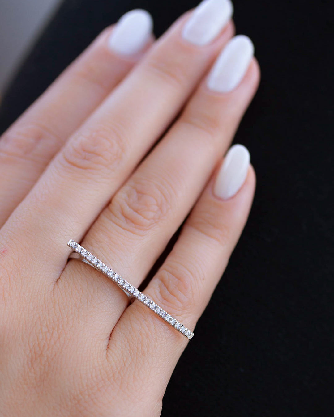 A dainty 14k white gold two finger ring, with a long bar set with white diamonds, that covers both fingers.